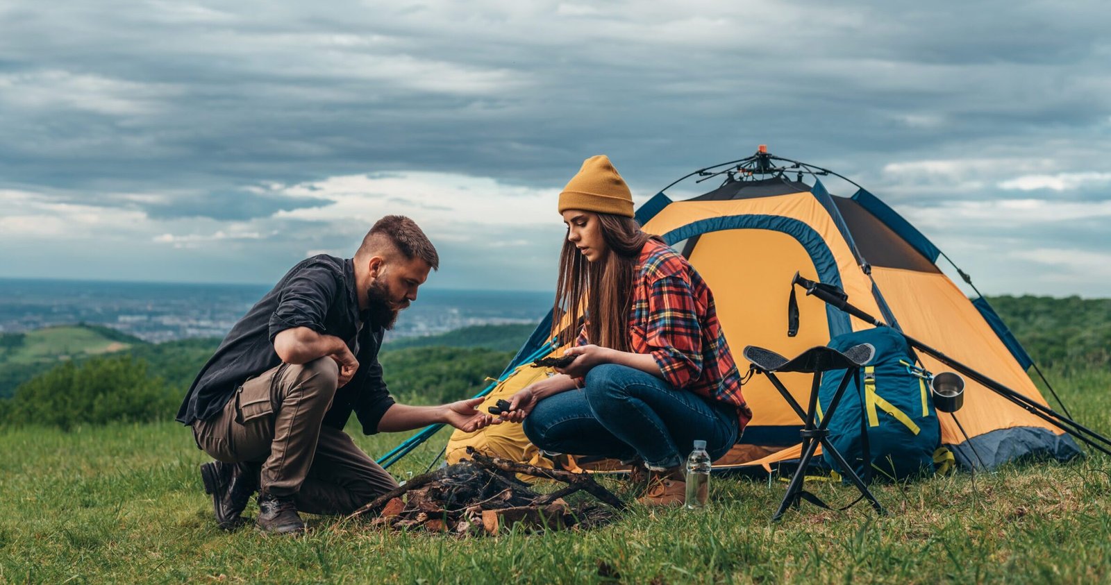 Couple of campers lighting a fire near the tent in a camp
